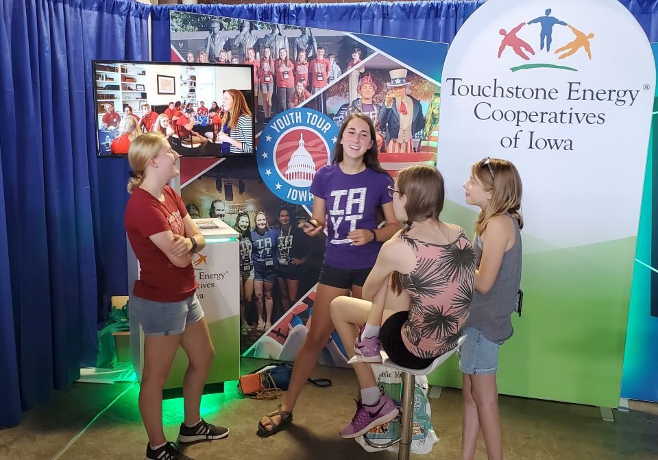 young fairgoers learning about cooperative leadership programs from youth tour alumni while standing in the booth