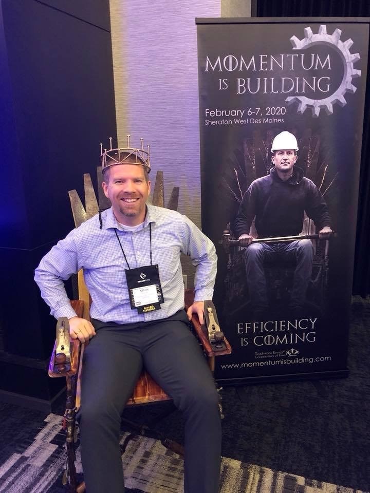 Photo of the Momentum is Building event banner and the specially-designed and adapted throne with a man sitting in it, wearing a crown.