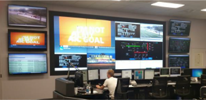 Photo image of a control operator, seated at a desk, with multiple 55-inch monitors in front of him, displayed on a wall.