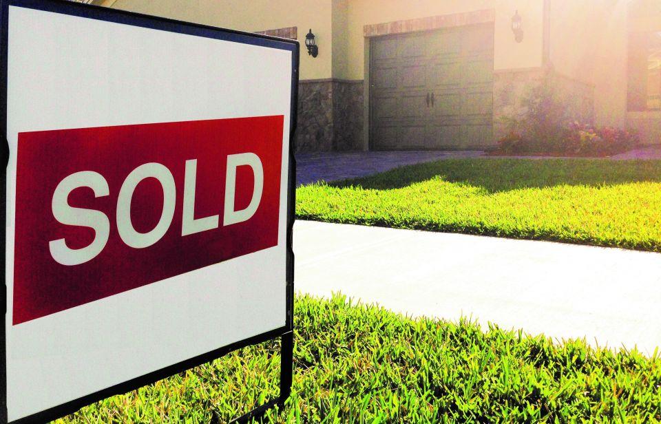 Real estate sign in the lawn of a home with the word "SOLD" on it