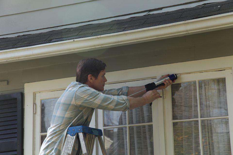 Photo of man caulking windows of his home