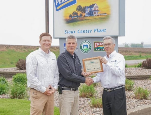Representatives from NIPCO, Perdue Premium Meats, and North West REC pose in front of the Perdue Premium Meats Company sign, holding the framed renewable energy credt certificate