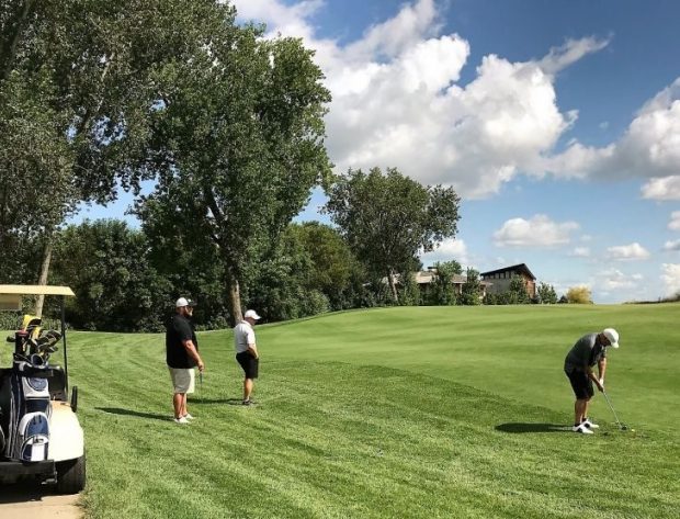 Long shot of a golf team with a player swinging a club on the golf fairway