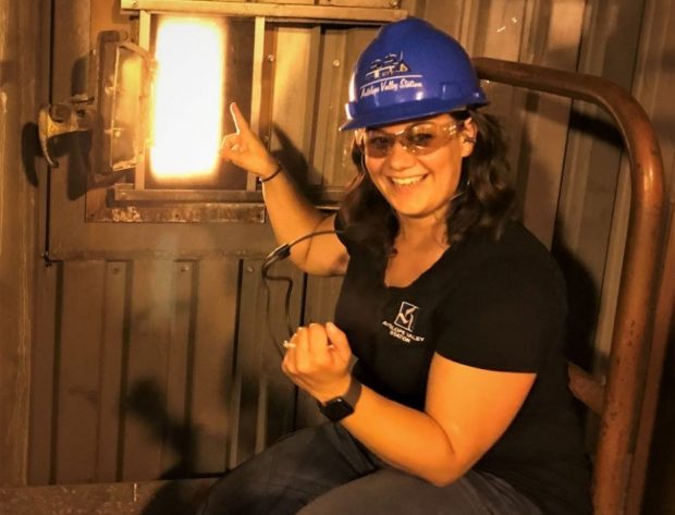 A female tour guide wearing a hard hat points at a window into the coal boiler at Antelope Valley Station