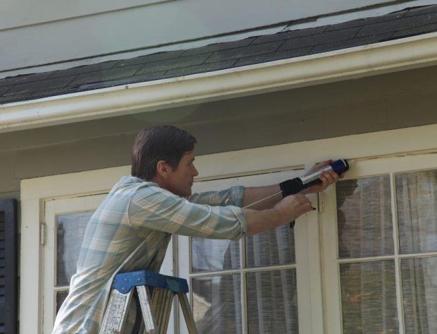 Photo of man caulking windows of his home