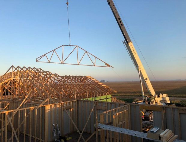 Photo of crane lifting roof truss to a house top