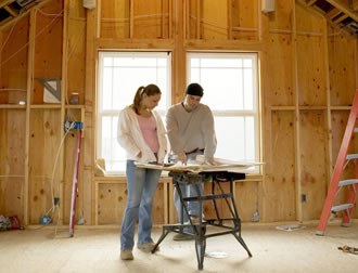 Image features a young woman and young man studying architectural plans in an unfinished area of a home.
