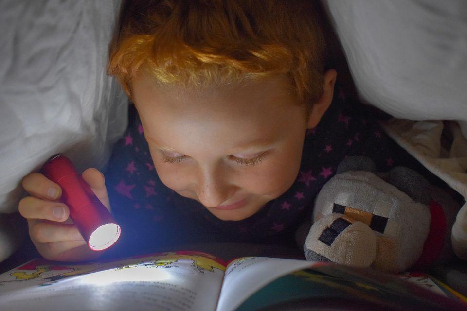 child reading by flashlight under a blanket