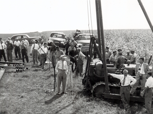 Image is a photo taken of the first pole setting with NIPCO representatives and onlookers.