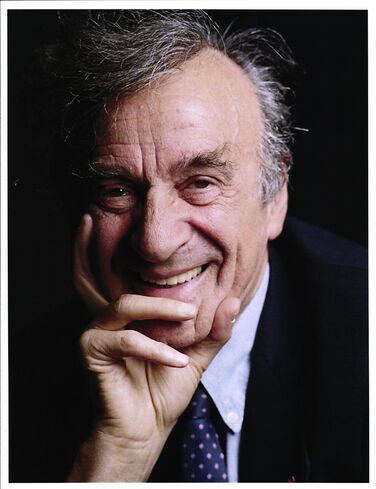 Color photograph of Elie Wiesel, smiling at the camera with his fingers on his chin.