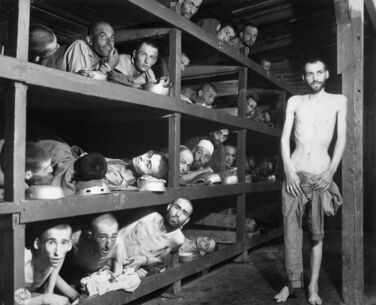Four stories of emaciated men on wooden bunks, with a mostly naked man in the foreground on the right.