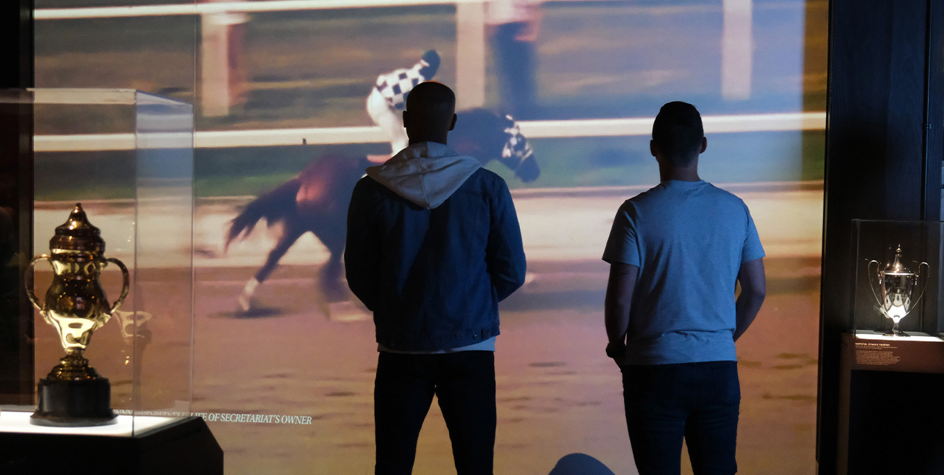 adults watching a horse racing film at the museum
