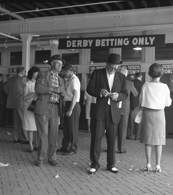 Vintage black and white image of people placing wagers at the betting booths at the track