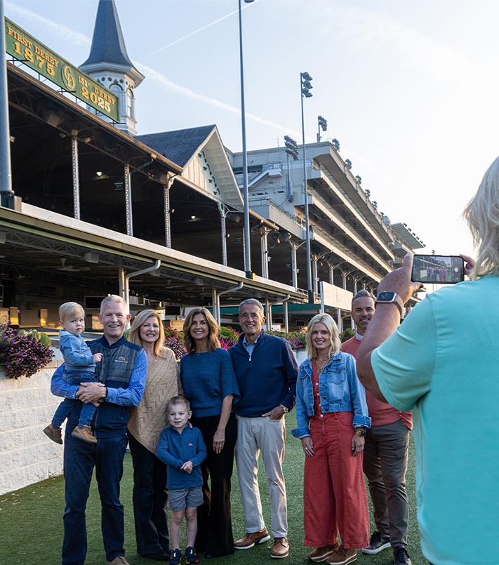 Family taking group photo with Twin Spires at Churchill Downs Racetrack