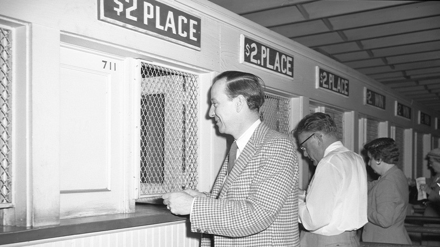 Vintage black and white image of people placing wagers at the betting booths at the track