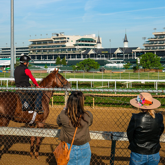 two women taking pictures of a jockey on its horse during the backstretch workout tour