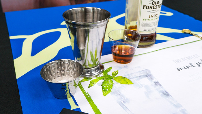 mint, sugar, silver julep cup, bourbon sample, and bourbon bottle on a table