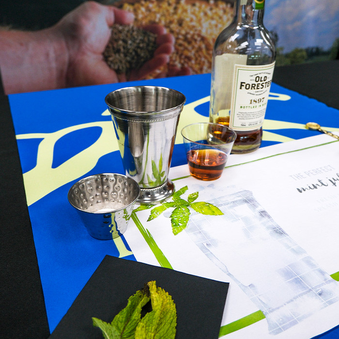 mint, sugar, silver julep cup, bourbon sample, and bourbon bottle on a table
