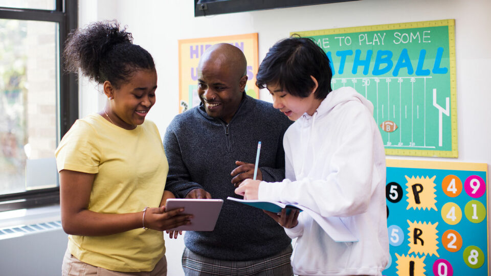 Teacher standing with two students holding a tablet
