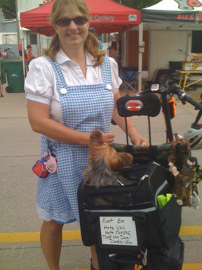 Dressed like Dorothy of Oz, a rider totes her Toto on the back of her cycle