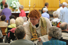 The Rev. Dr. Georgine Buckwalter serves communion to a wheelchair-bound congregant at St. Luke's chapel