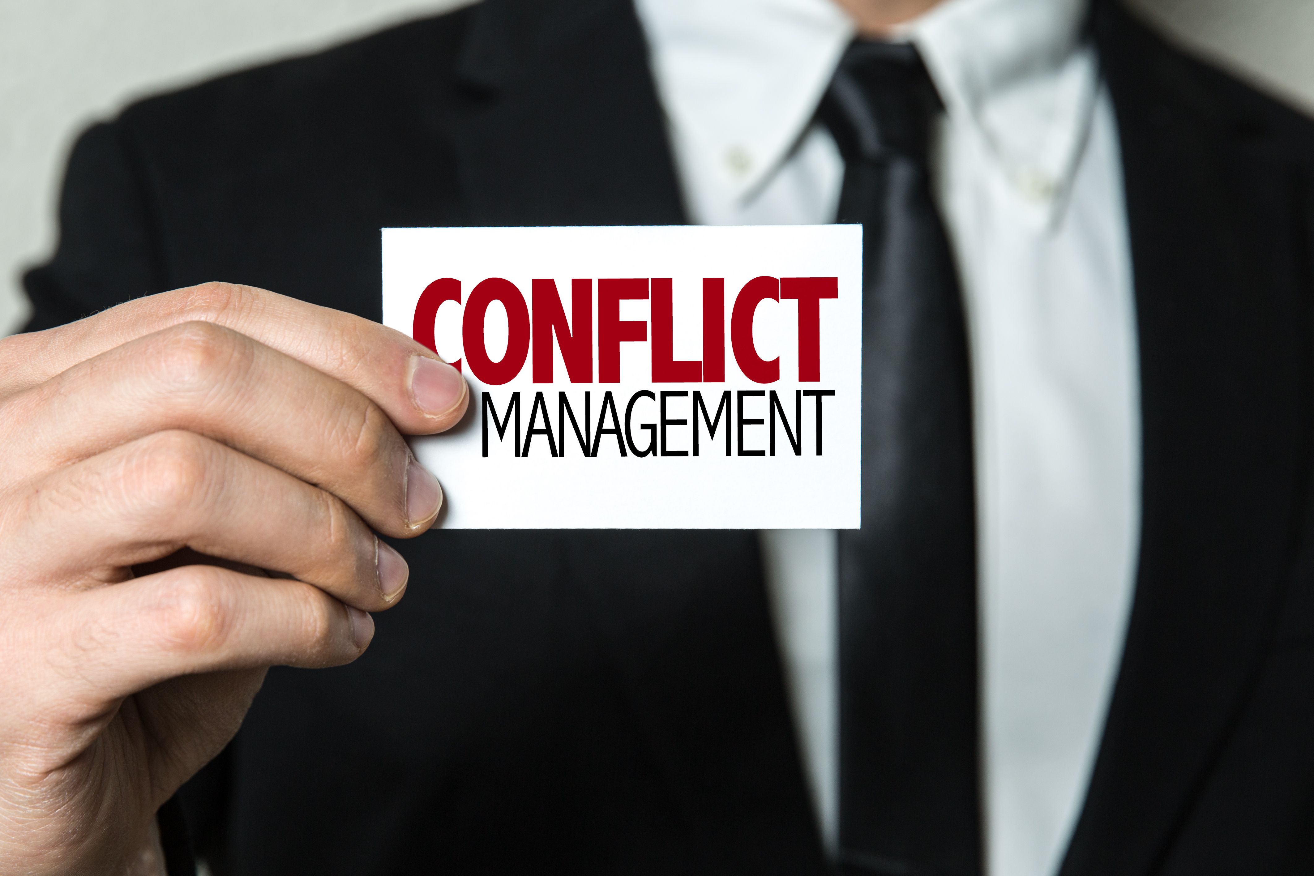 A close-up on a business man holding a small sign that reads, Conflict Management.