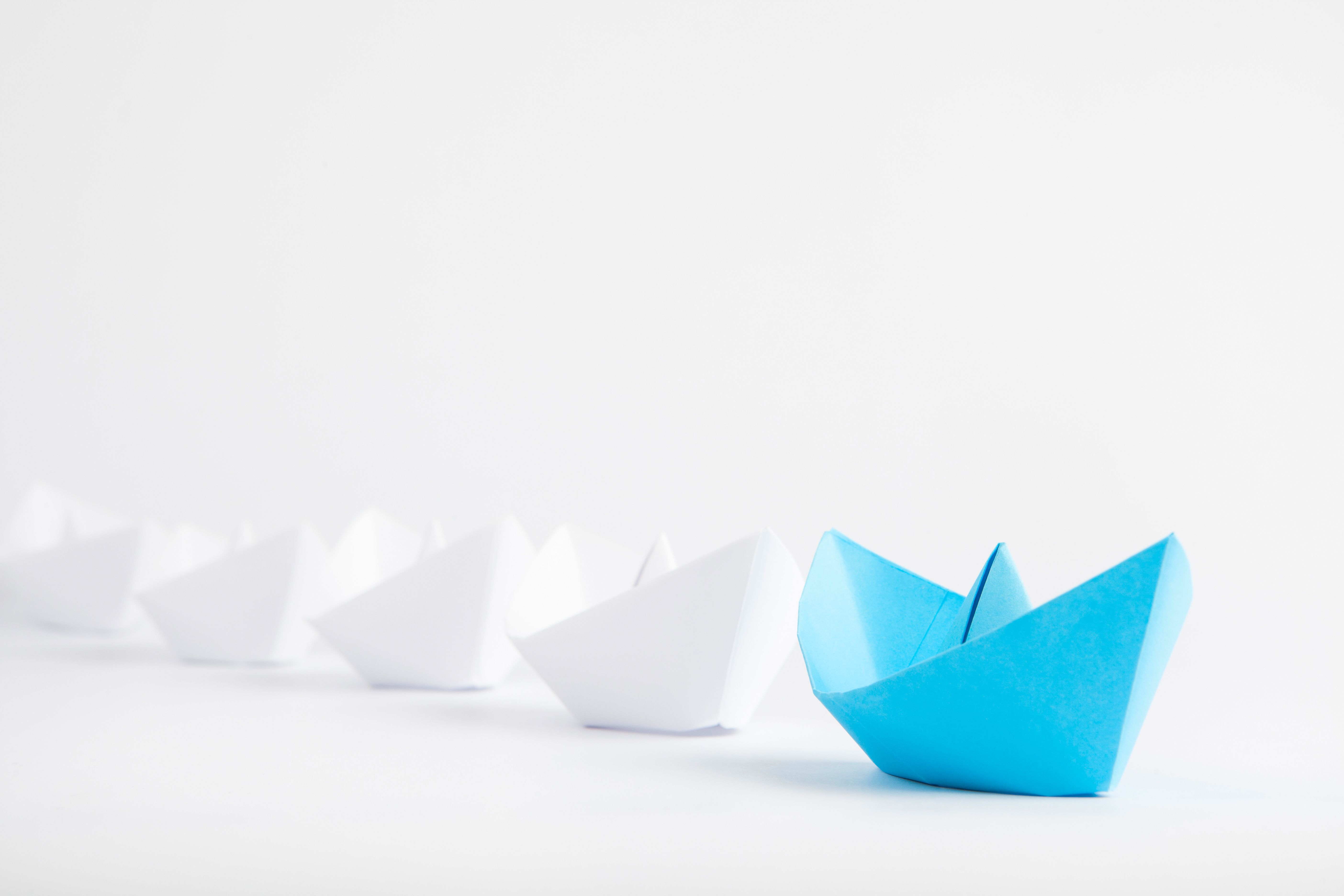 Leadership concept, represented by a blue paper ship leading a row of white paper ships