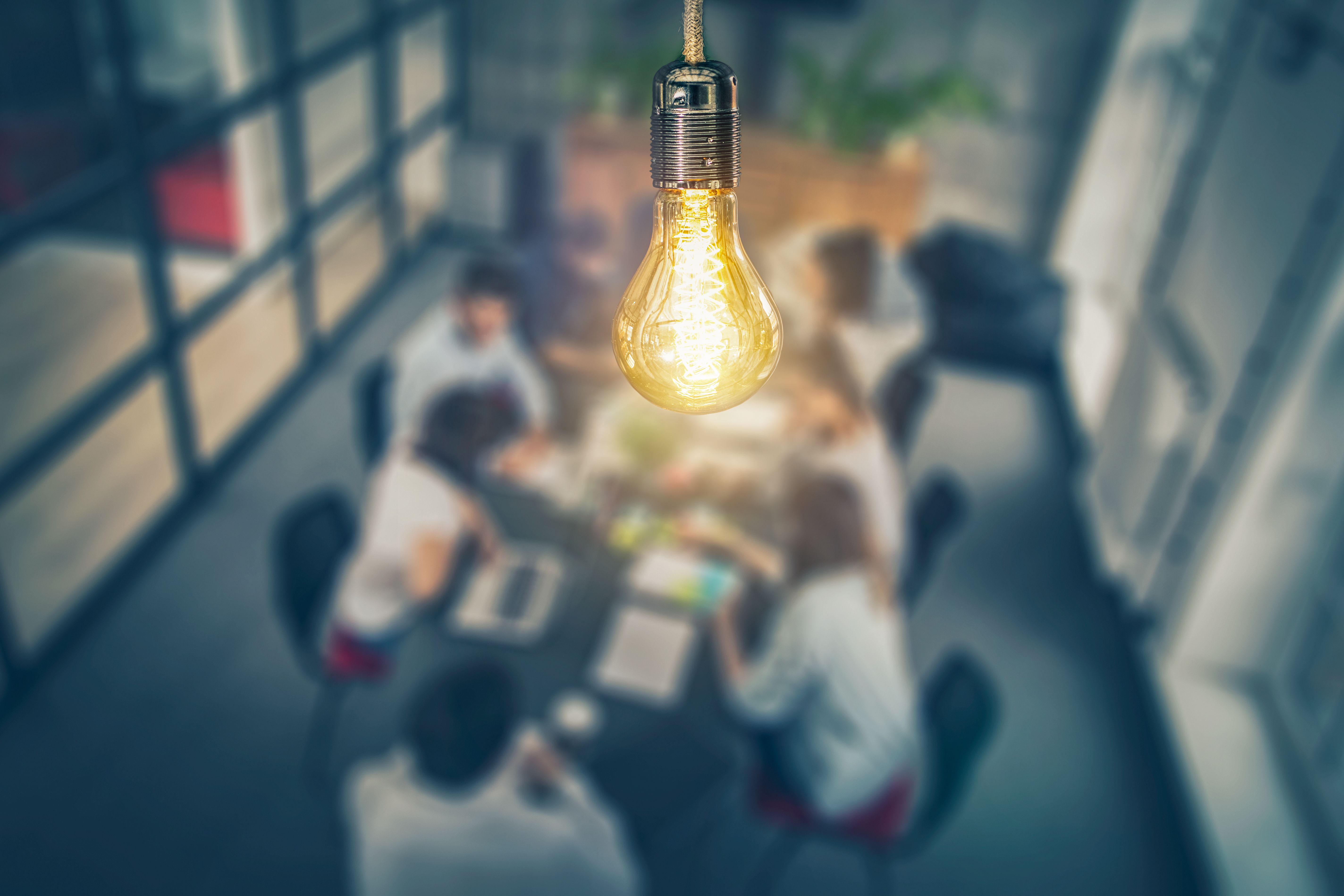 A glowing light bulb, above a group of people working in an office, represents ideas.
