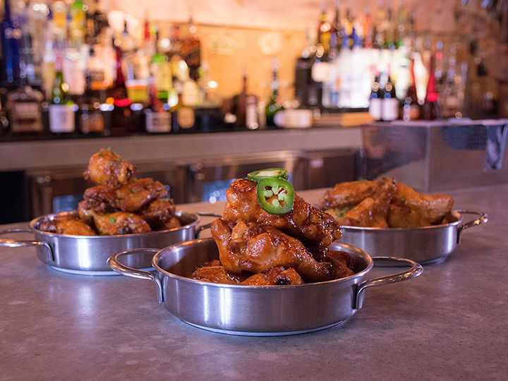 Three serving pans of Wu Han’s Hot Wings on a bar counter at Jock Lindsey’s Hangar Bar