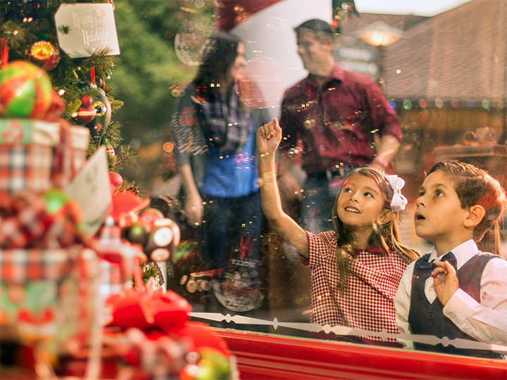 Two young children look in awe at a decorated Christmas tree on display in a shop window at Disney Springs