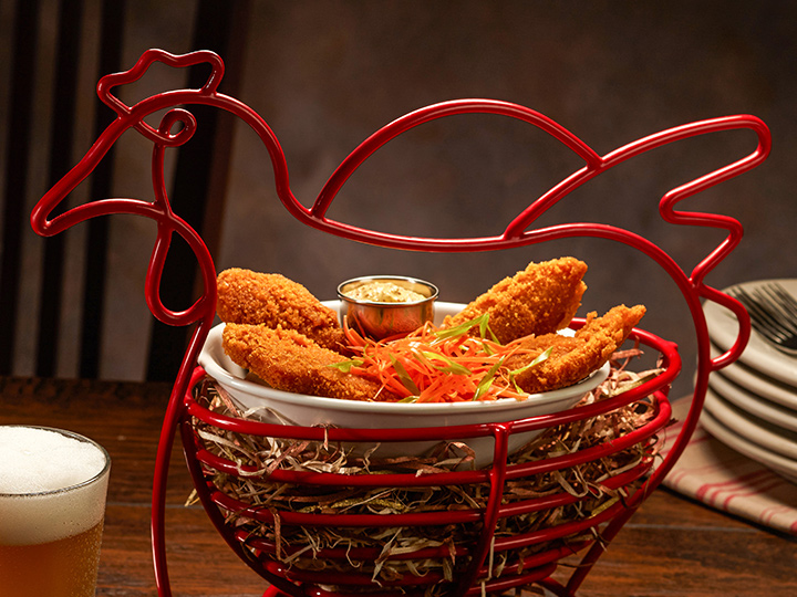 Chicken tenders inside a wire basket shaped like a chicken next to a glass of beer