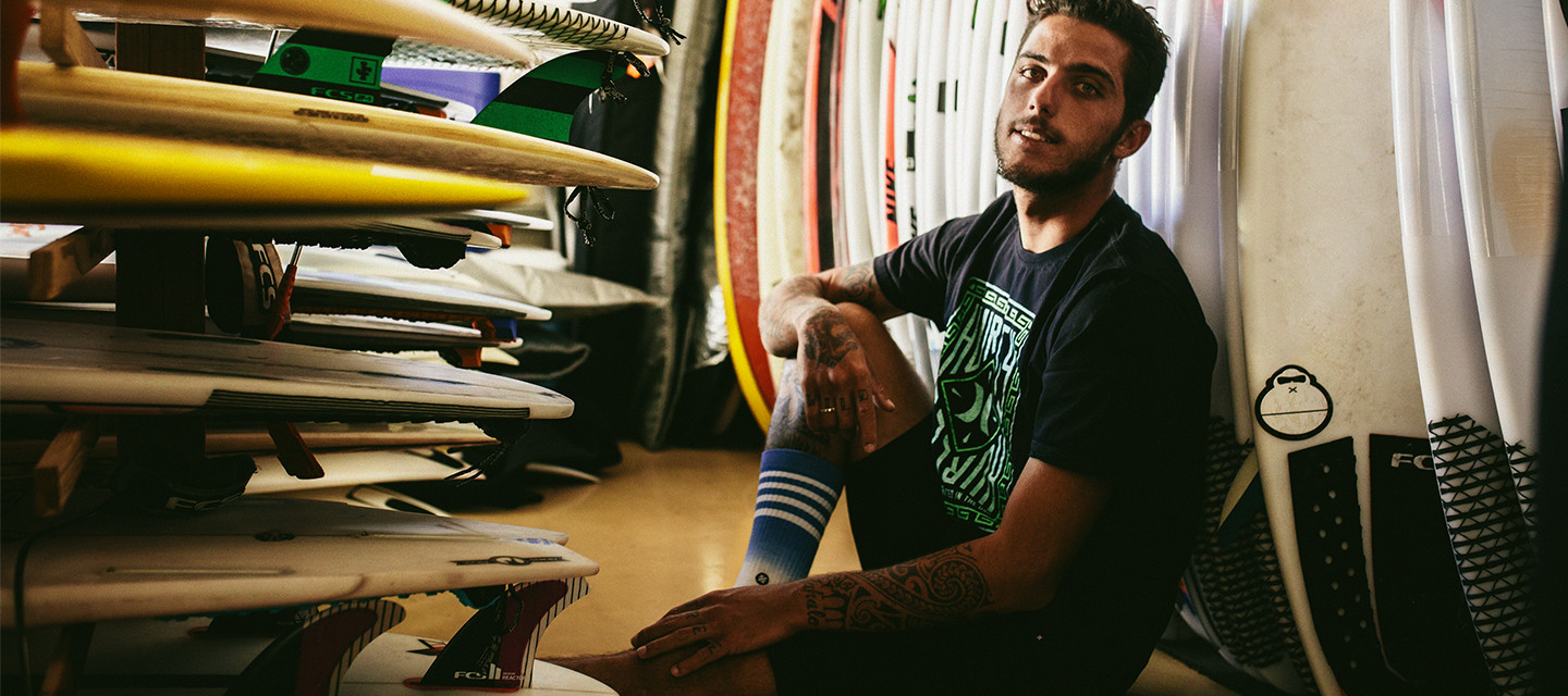 A man wearing Stance socks sits and leans against a row of surfboards