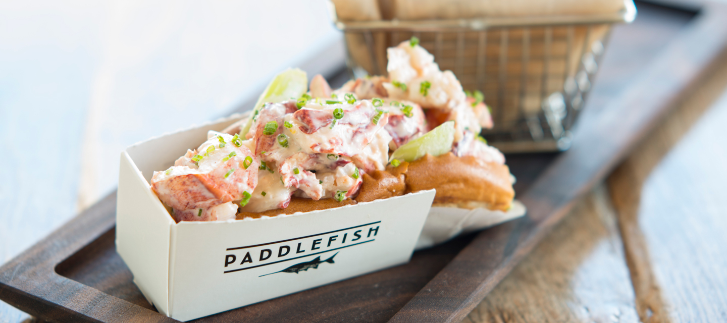 A lobster roll in a Paddlefish logo box next to a basket of French fries at Disney Springs