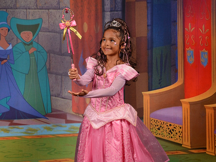 A young girl dressed as Aurora poses against a Sleeping Beauty themed digital backdrop