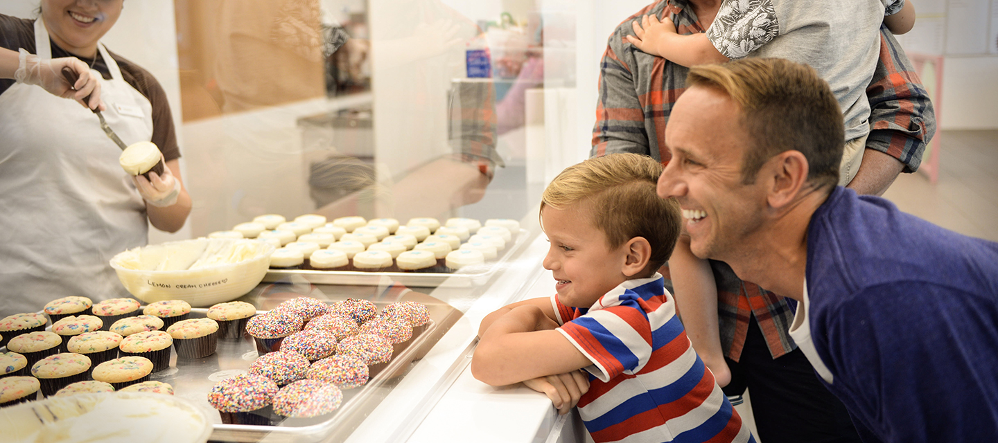 Two dads and their young sons peer through the display glass at Sprinkles cupcakes