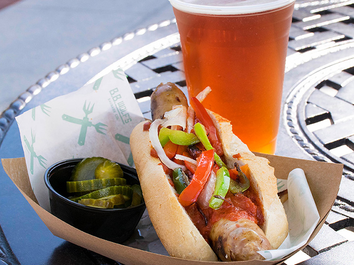 An Italian sausage with a side of pickles and a draft beer