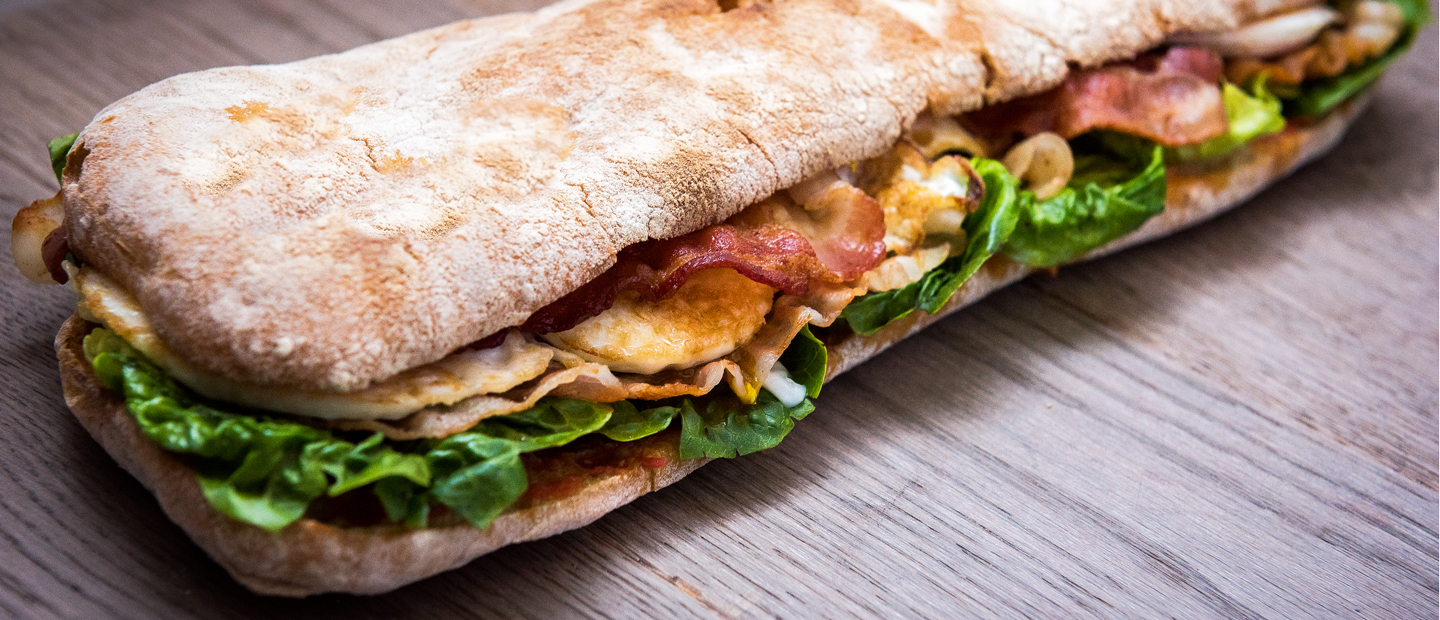 A long sandwich with thin bread, bacon, lettuce and other ingredients
