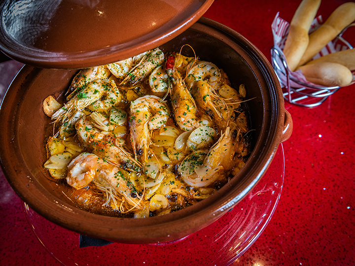 Prawns cooked in their shells served with herbs and sliced garlic in a round dish