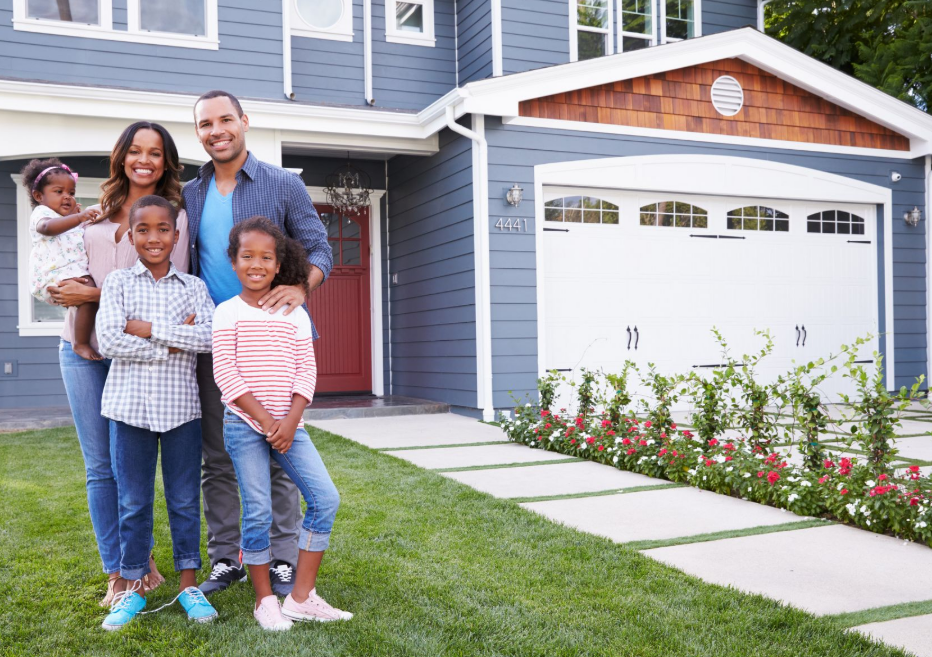 A happy family poses in front of their beautiful, modern suburban home