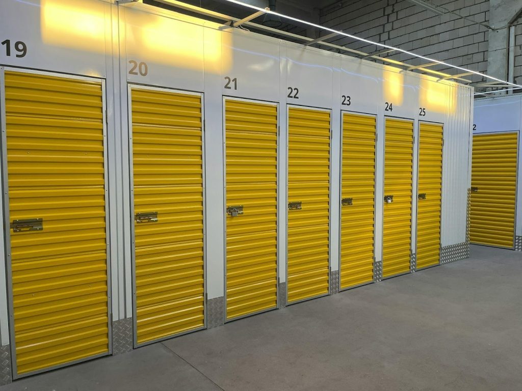 A row of yellow storage unit doors inside a clean indoor storage facility, each numbered for identification.