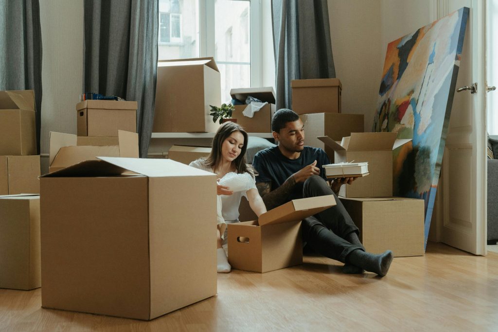 Couple unpacking cardboard boxes in a new apartment, surrounded by moving supplies