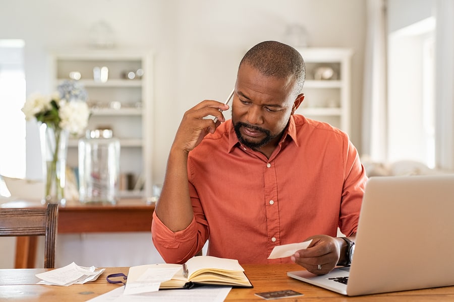 Man sitting at a desk on the phone, paying bills.