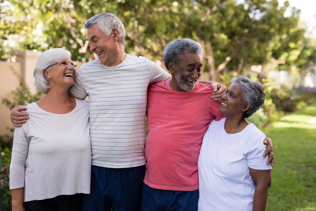 Happy senior couple with friends standing at park