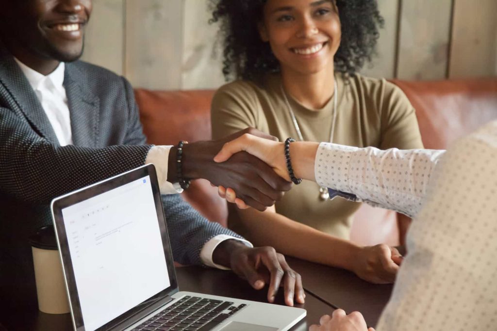 Couple shaking hands with business person at a laptop.