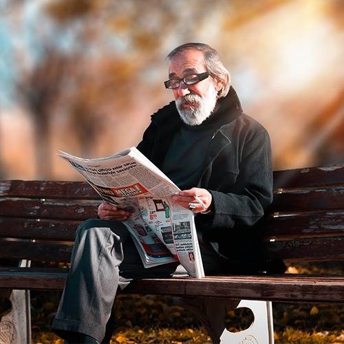 Old man sitting on bench reading newspaper