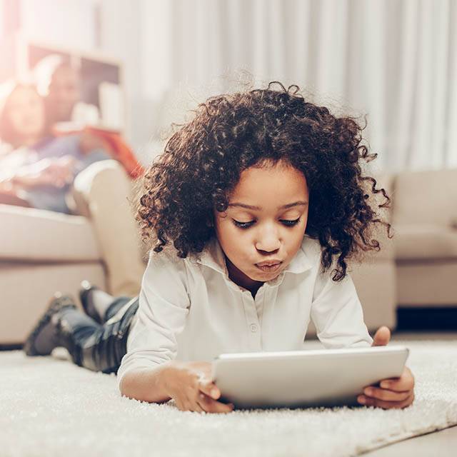 Thoughtful Kid Looking At Tablet While Resting On Soft Tapis Ins