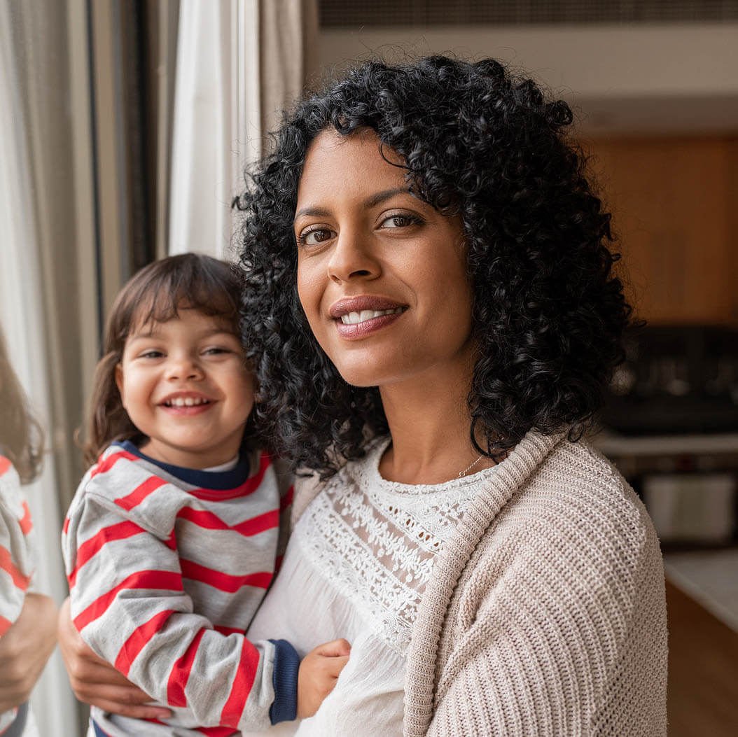 Smiling Mother And Daughter Standing By Their Living Room Window