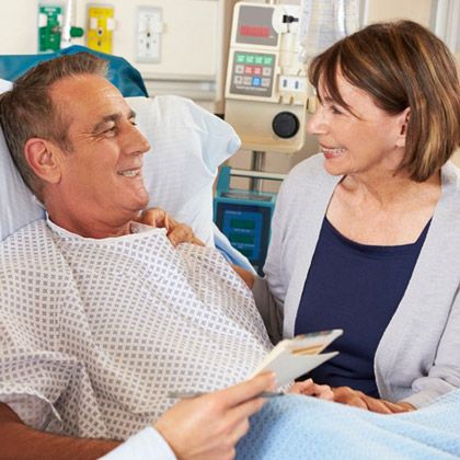 Smiling husband in hospital bed holding paperwork and talking to wife