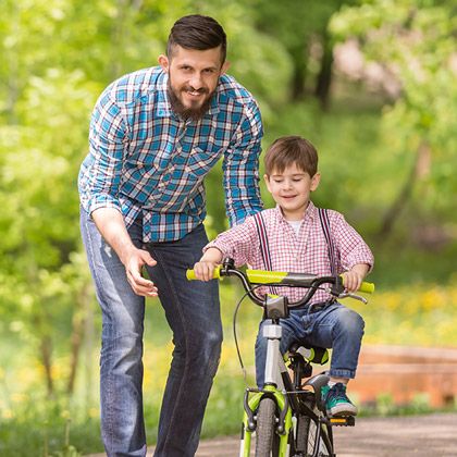 Dad reaching young son to ride a bike