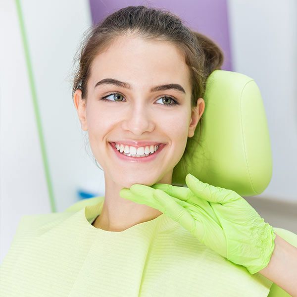Smiling woman in green dental bib with green gloved hand on chin
